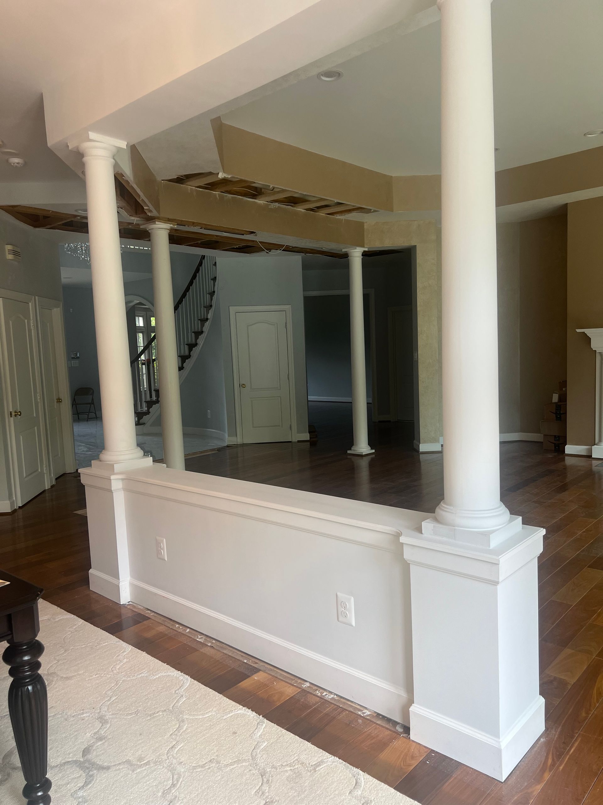 Interior room with white columns, half wall, hardwood floors, and a staircase in the background