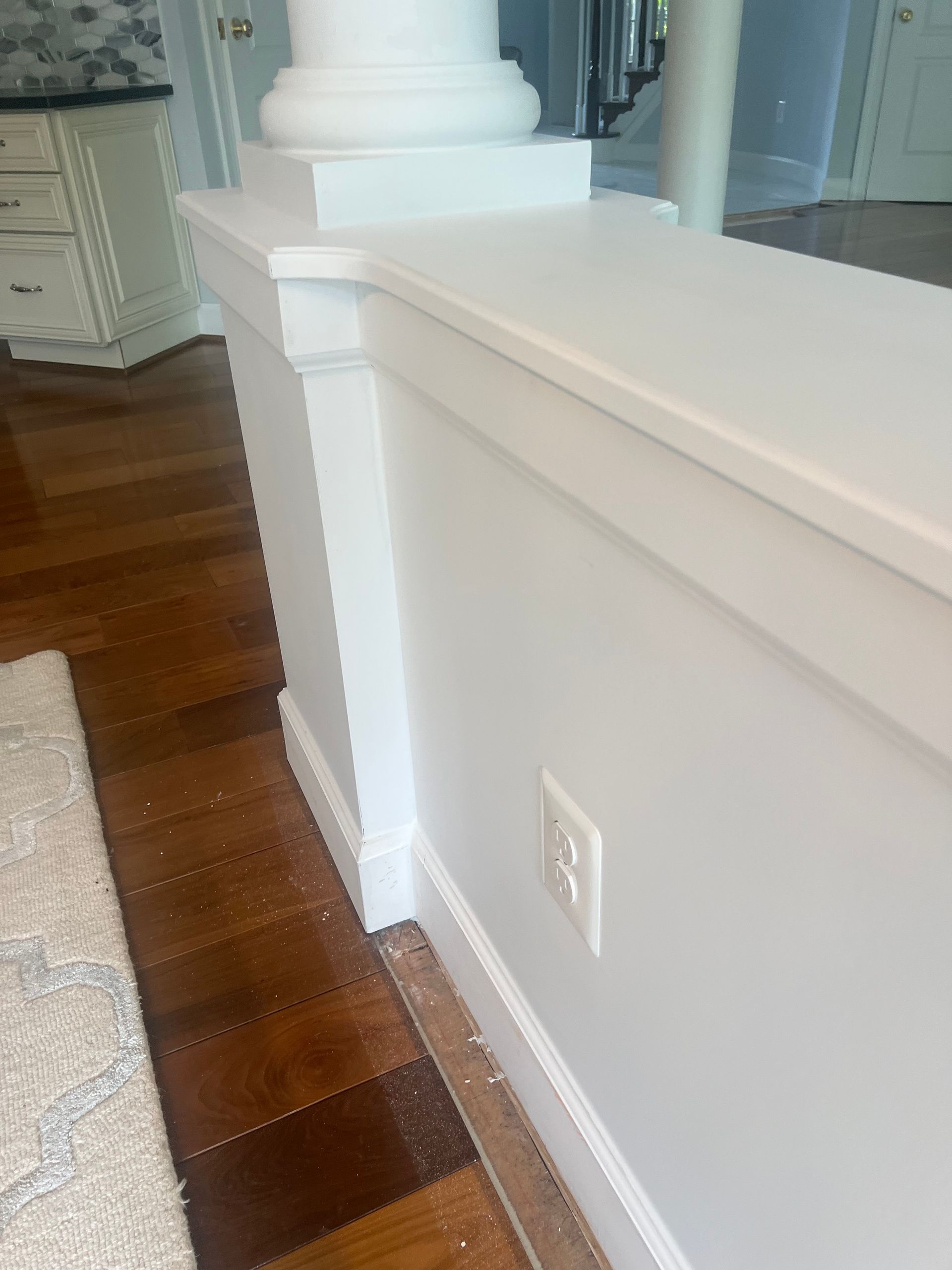 White wainscoted wall by hardwood floor, with a column and outlet in a bright interior room