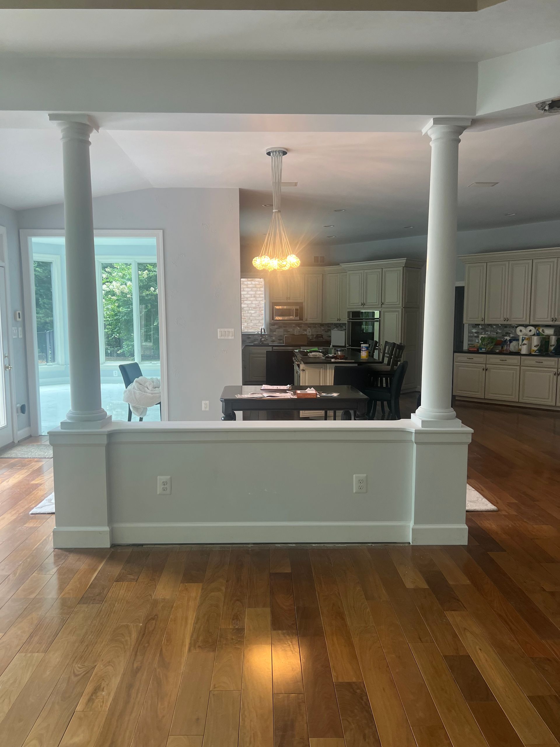 Open living-dining area with hardwood floors, white columns, and a chandelier visible through a wide pass-through.