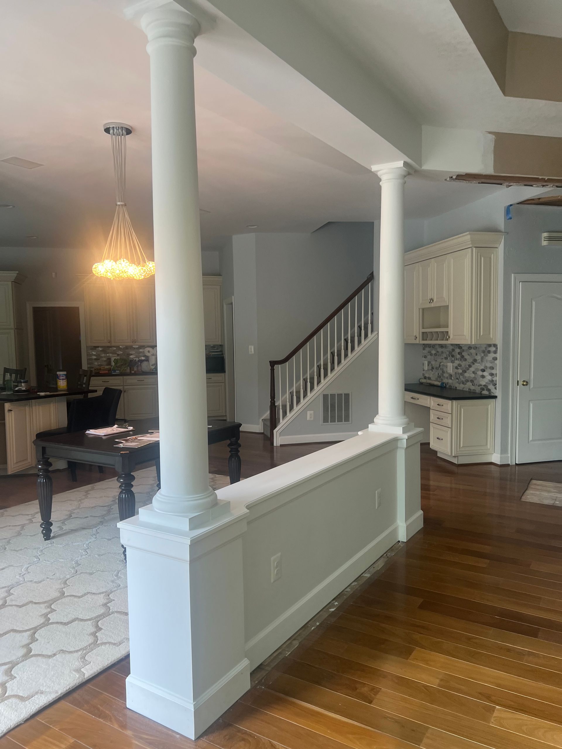 Elegant foyer with white columns, staircase, chandelier, and hardwood floors, opening to a living area
