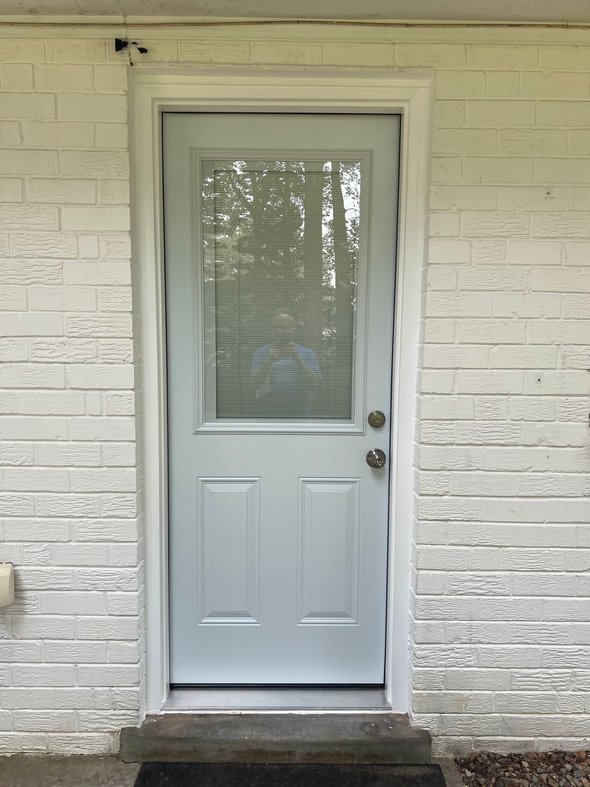 White exterior door with frosted window in a white brick wall
