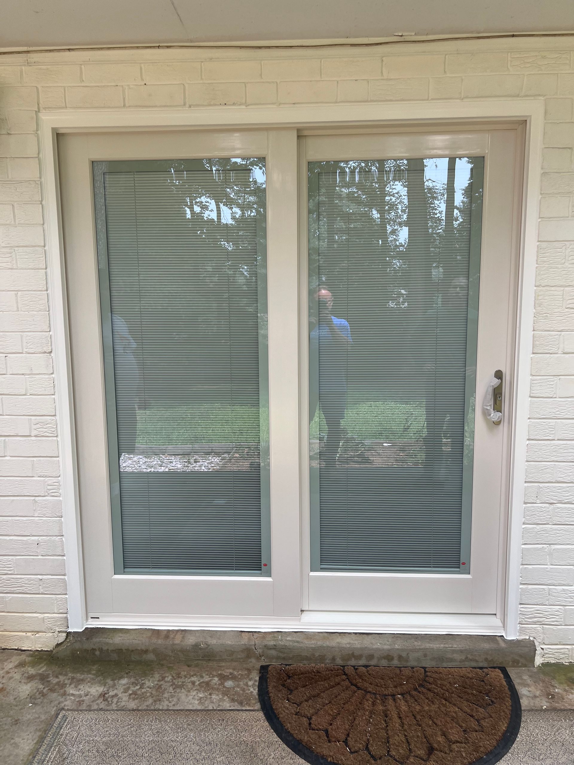 White sliding glass patio door with closed blinds and a doormat on a stone step
