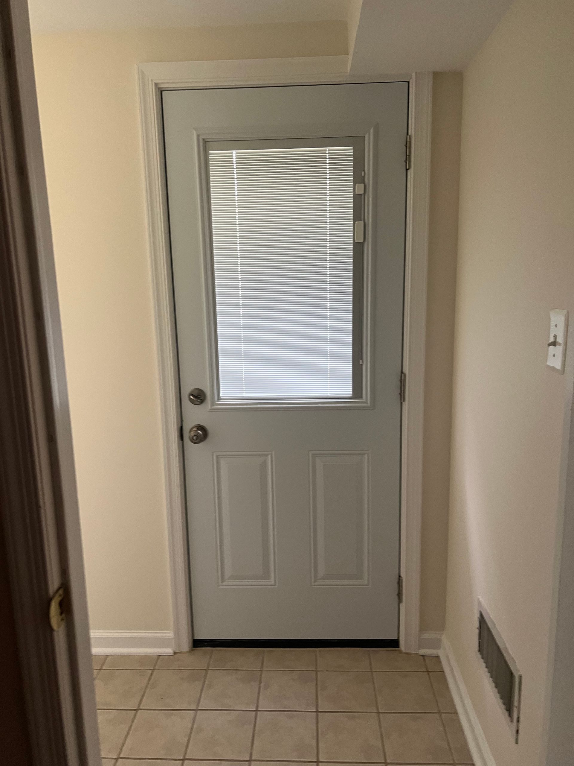 Interior view of a white back door with frosted glass, tiled floor, and beige walls in a hallway