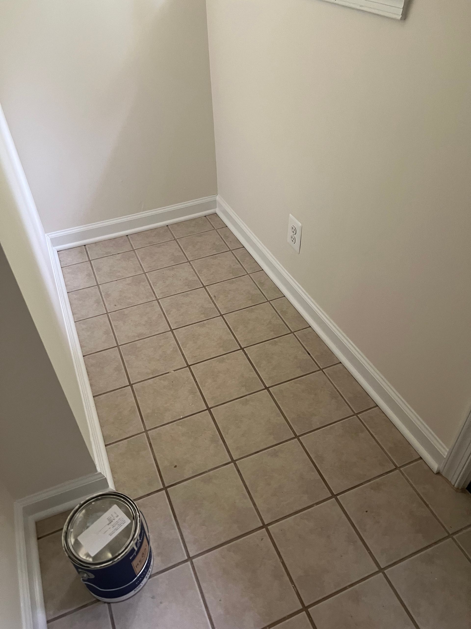 Empty tiled hallway corner with white walls and a paint can on the floor