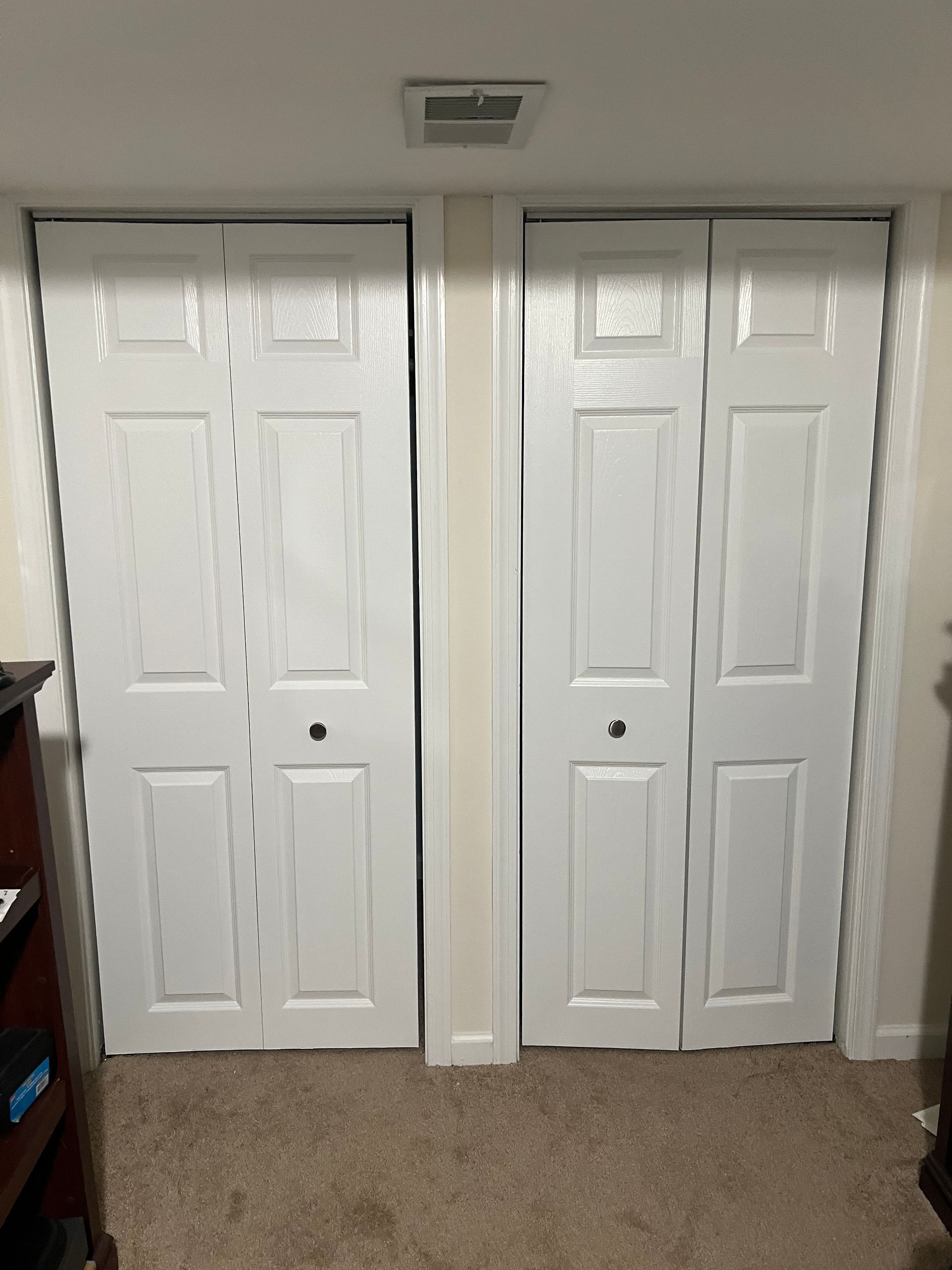 White double closet doors with round knobs in a beige-carpeted room, divided by a narrow wall column.