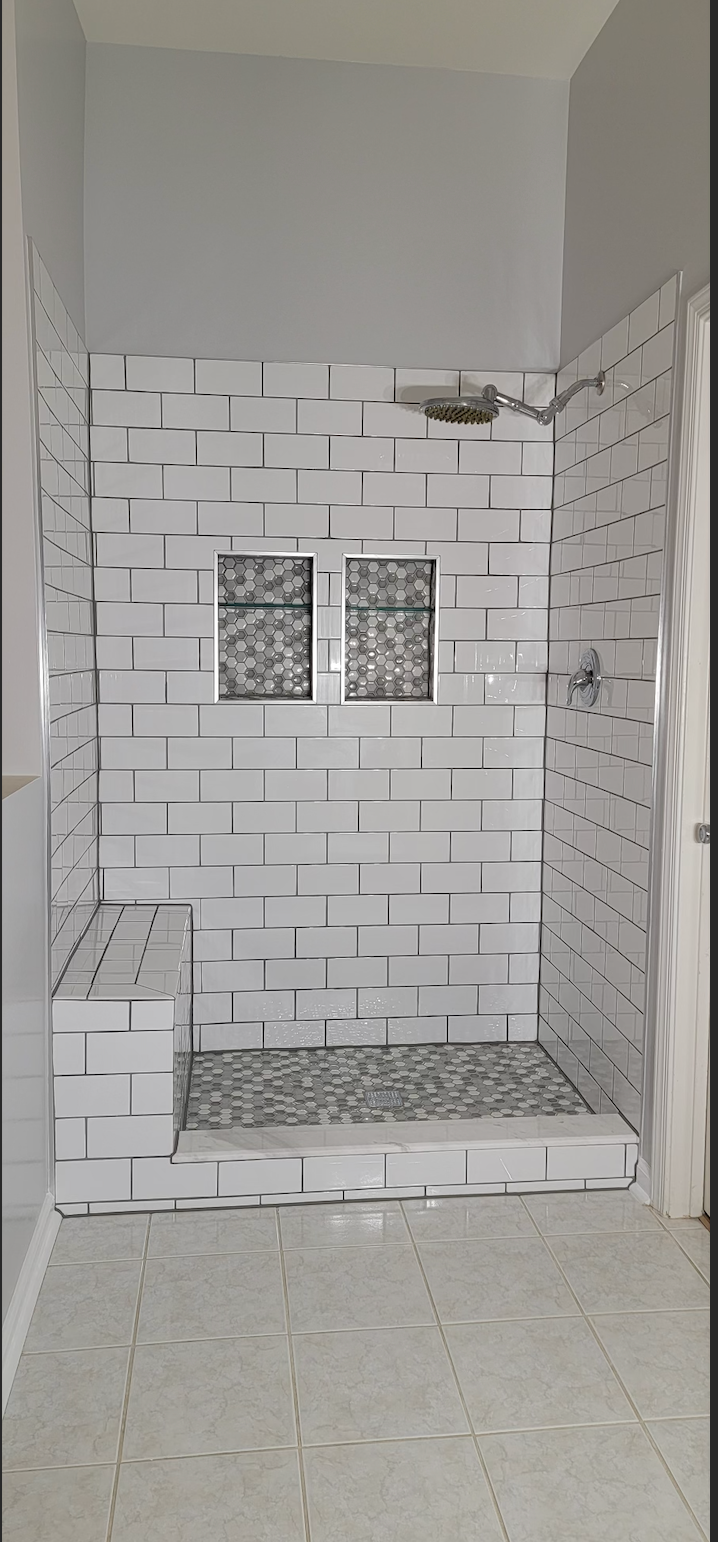 A bathroom with white tiles and a walk in shower.