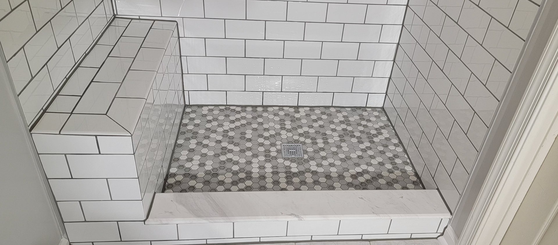 A bathroom with white tiles and a walk in shower with a bench.