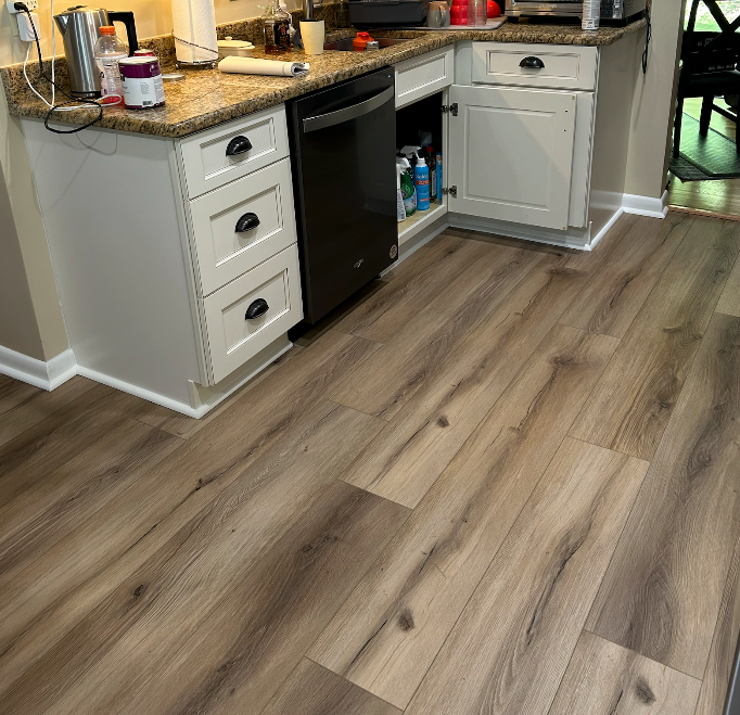 A kitchen with hardwood floors , white cabinets , and a black dishwasher.