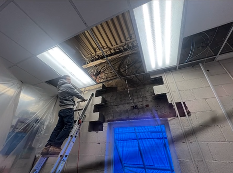 A man is standing on a ladder working on the ceiling of a building.
