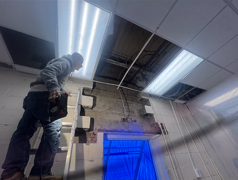 A man is standing on a ladder working on a light fixture in a room.