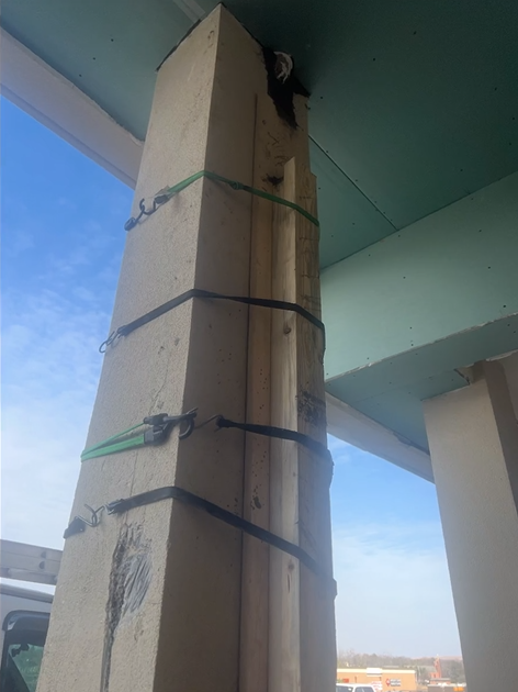 A concrete pole with straps around it is under a bridge.