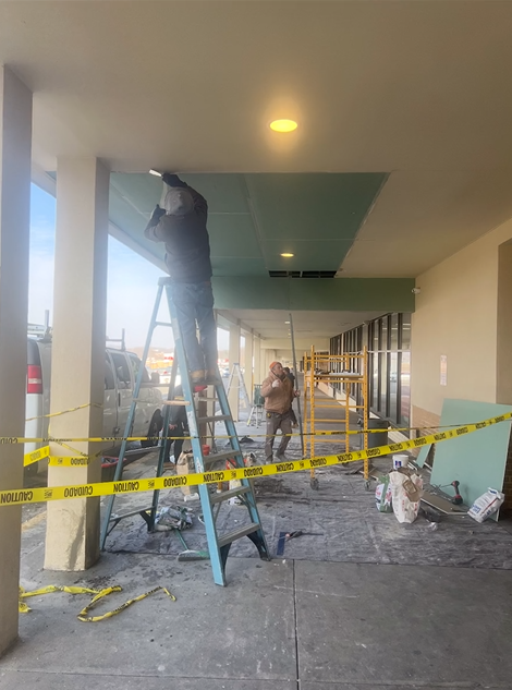 A man is standing on a ladder working on the ceiling of a building.