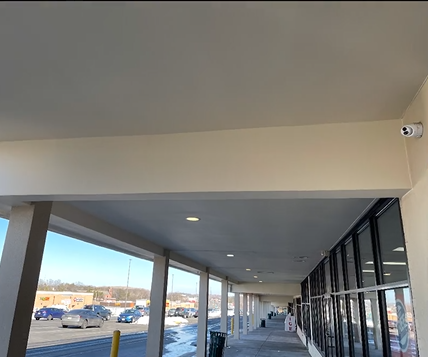A covered walkway between two buildings with cars parked in the background.