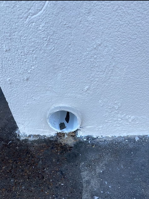 A white wall with a hole in it on the ground.
