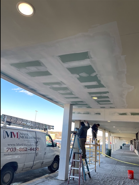 Two men are painting the ceiling of a building.