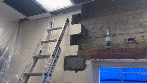 A ladder is sitting on top of a brick wall next to a window.