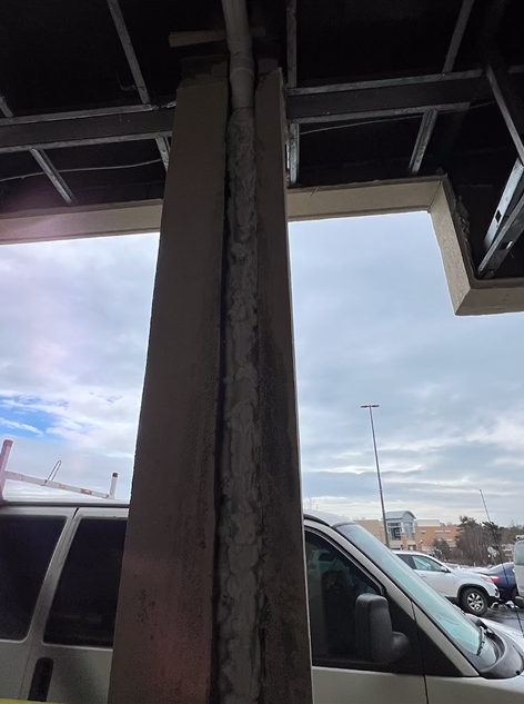 A white van is parked under a bridge in a parking lot