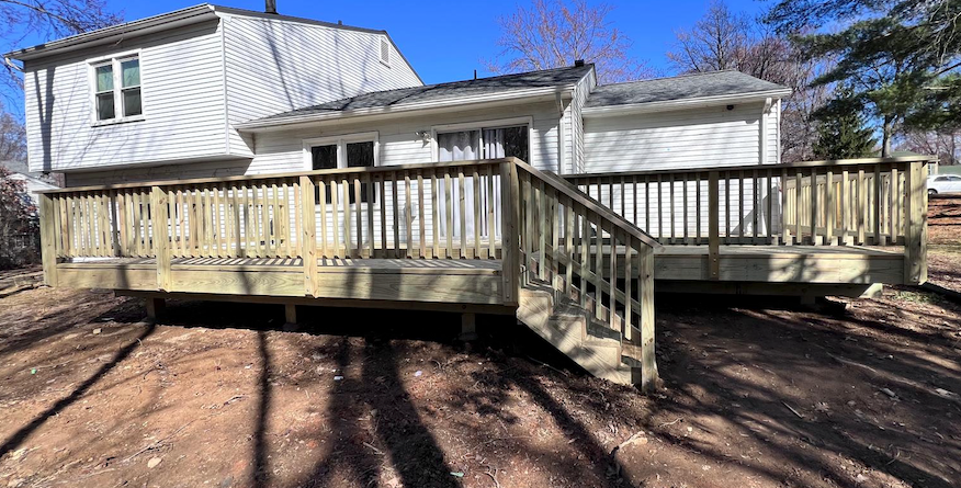 A large wooden deck with stairs is in front of a white house.