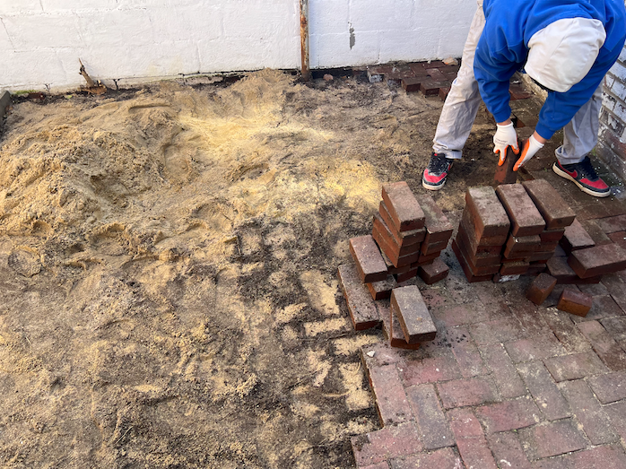 A man is laying bricks on a brick walkway.