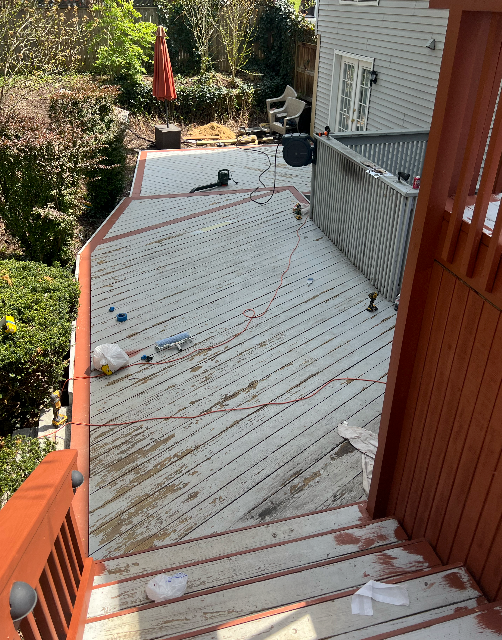 A wooden deck with stairs leading up to it and a house in the background.
