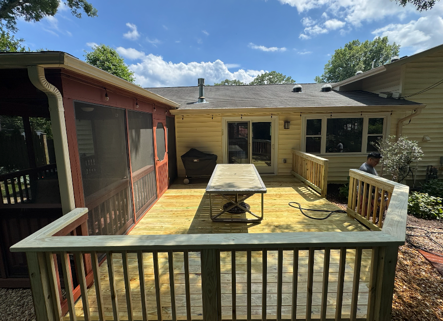 A wooden deck with a table and a screened in porch next to a house.