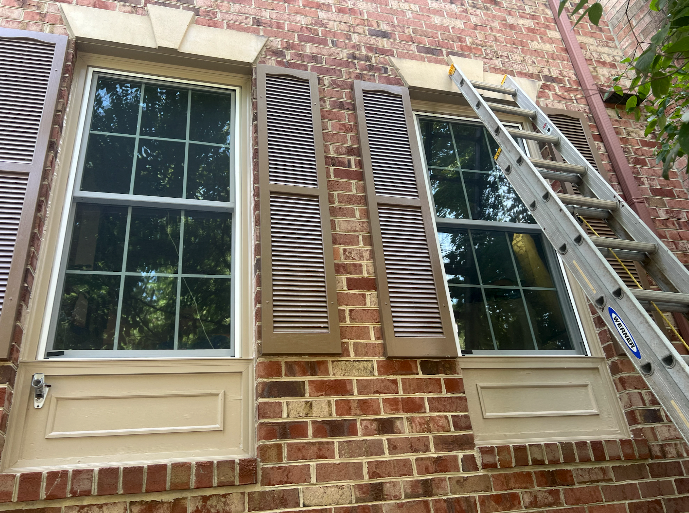 A ladder is leaning against a brick wall next to two windows.