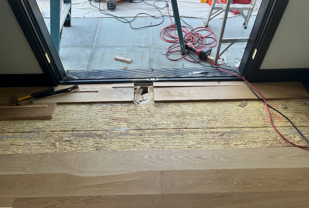 A wooden floor is being installed in a room next to a window.