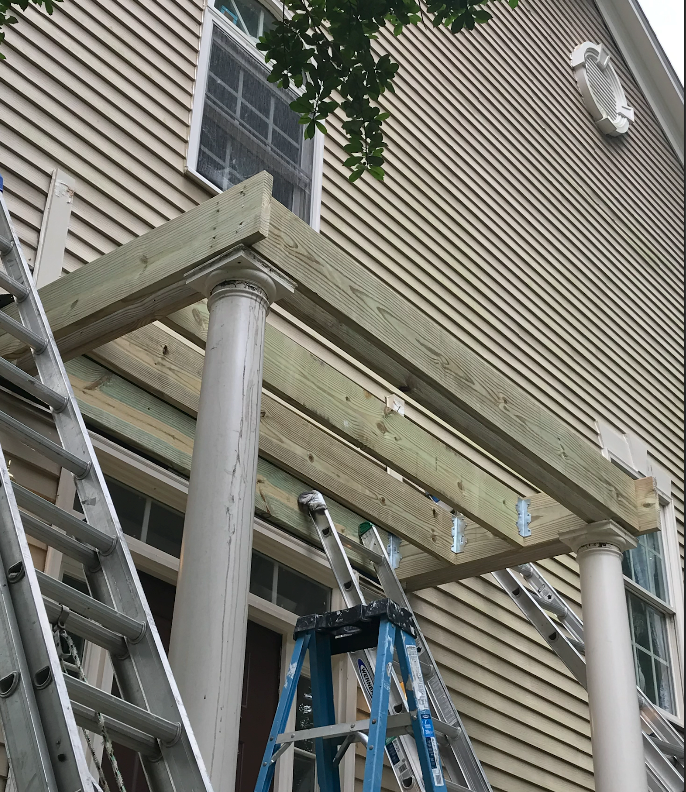 Construction of a porch roof in progress; lumber frame supported by white columns.