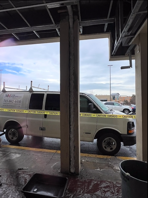 A white van is parked in a garage with yellow tape around it
