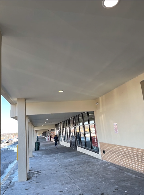 A person is walking down a sidewalk in front of a building.