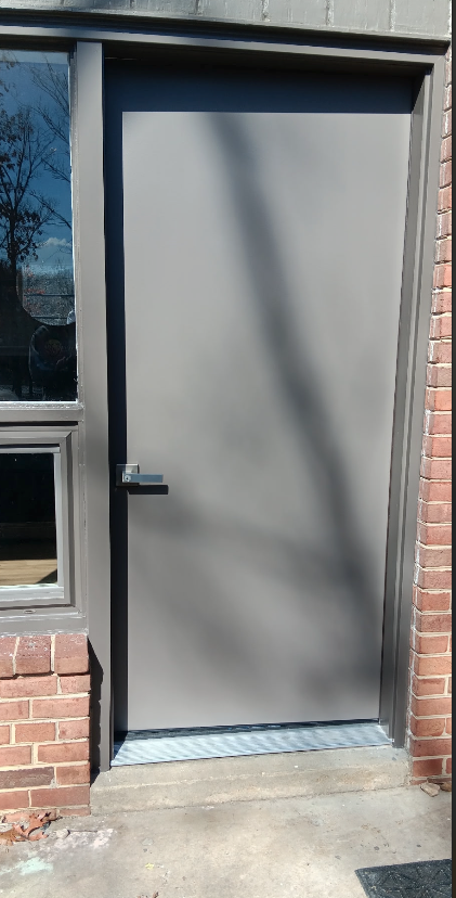 A gray door with a window on the side of a brick building.
