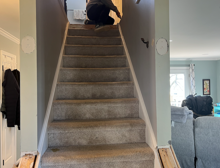 A person is kneeling down on the stairs in a living room.