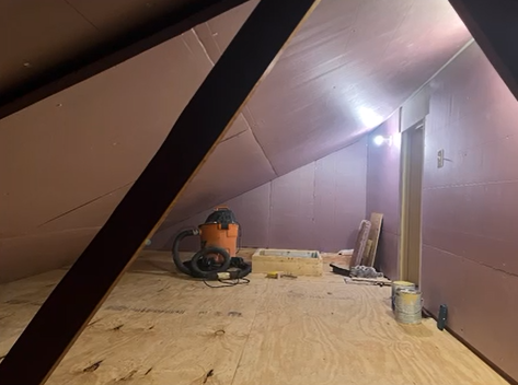 A vacuum cleaner is sitting on a wooden floor in an attic.