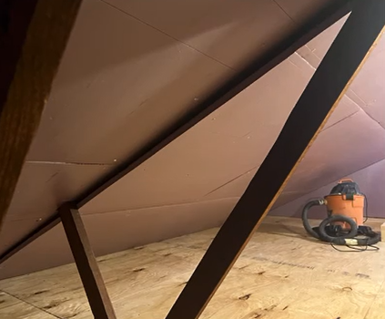 A vacuum cleaner is sitting on a wooden floor in an attic.