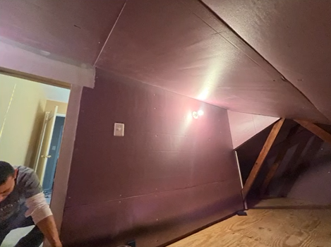 A man is working on a wall in an attic.