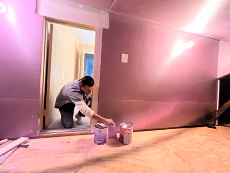 A man is kneeling down in a room holding a can of paint.