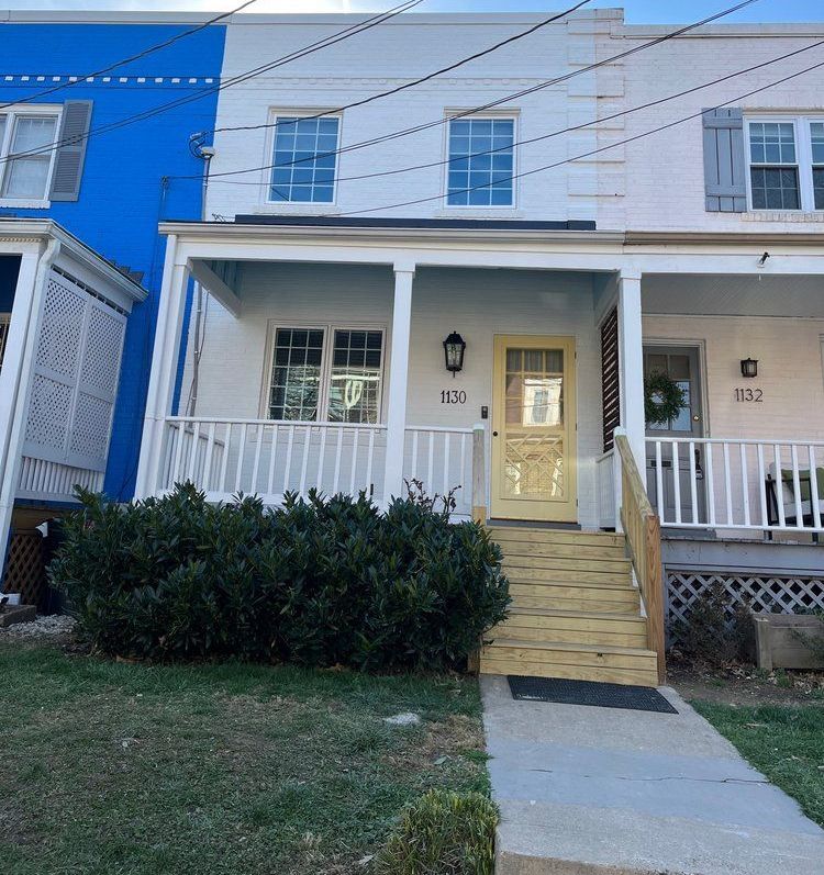 A white house with a porch and stairs is next to a blue house.