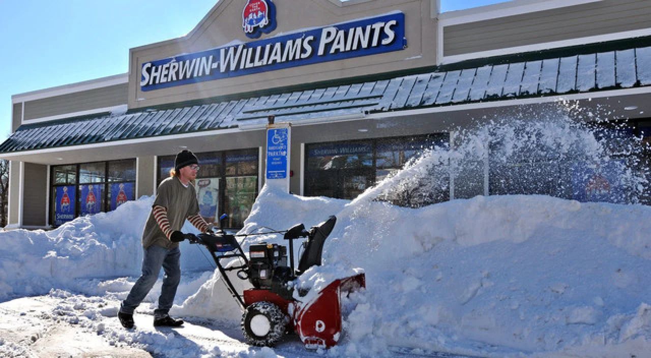 Man using a snowblower in front of a Sherwin-Williams store after heavy snowfall