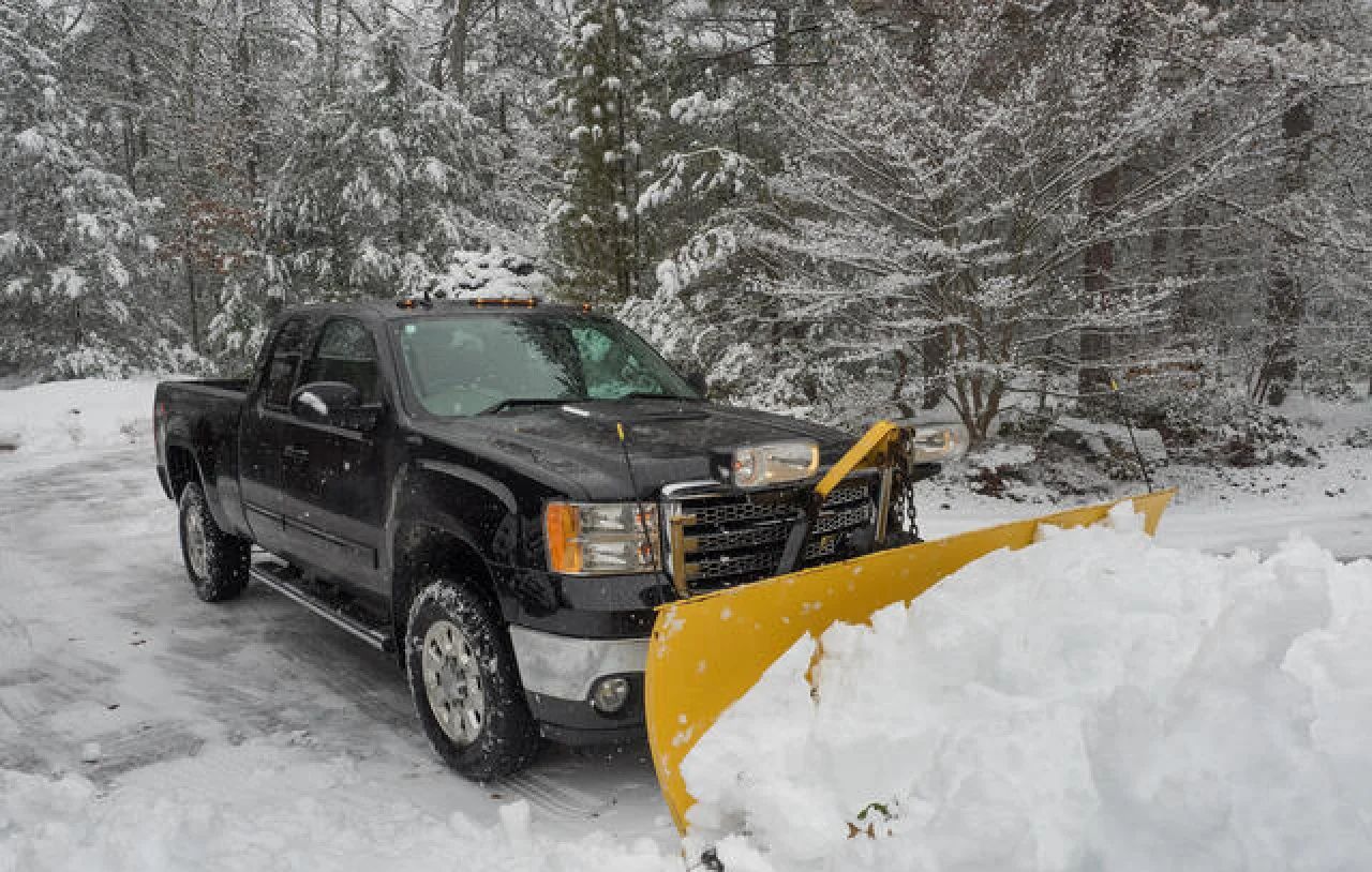 Black pickup truck plowing snow on a snowy road in front of trees