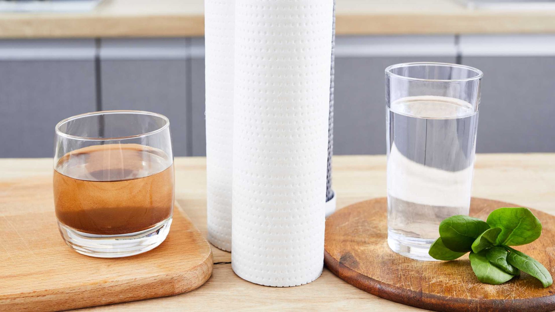 Two glasses on wooden coasters beside a white textured candle and mint leaves on a bright table