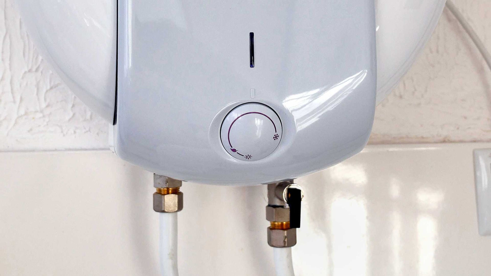 Close-up of a white water heater with a temperature dial and two pipes underneath.