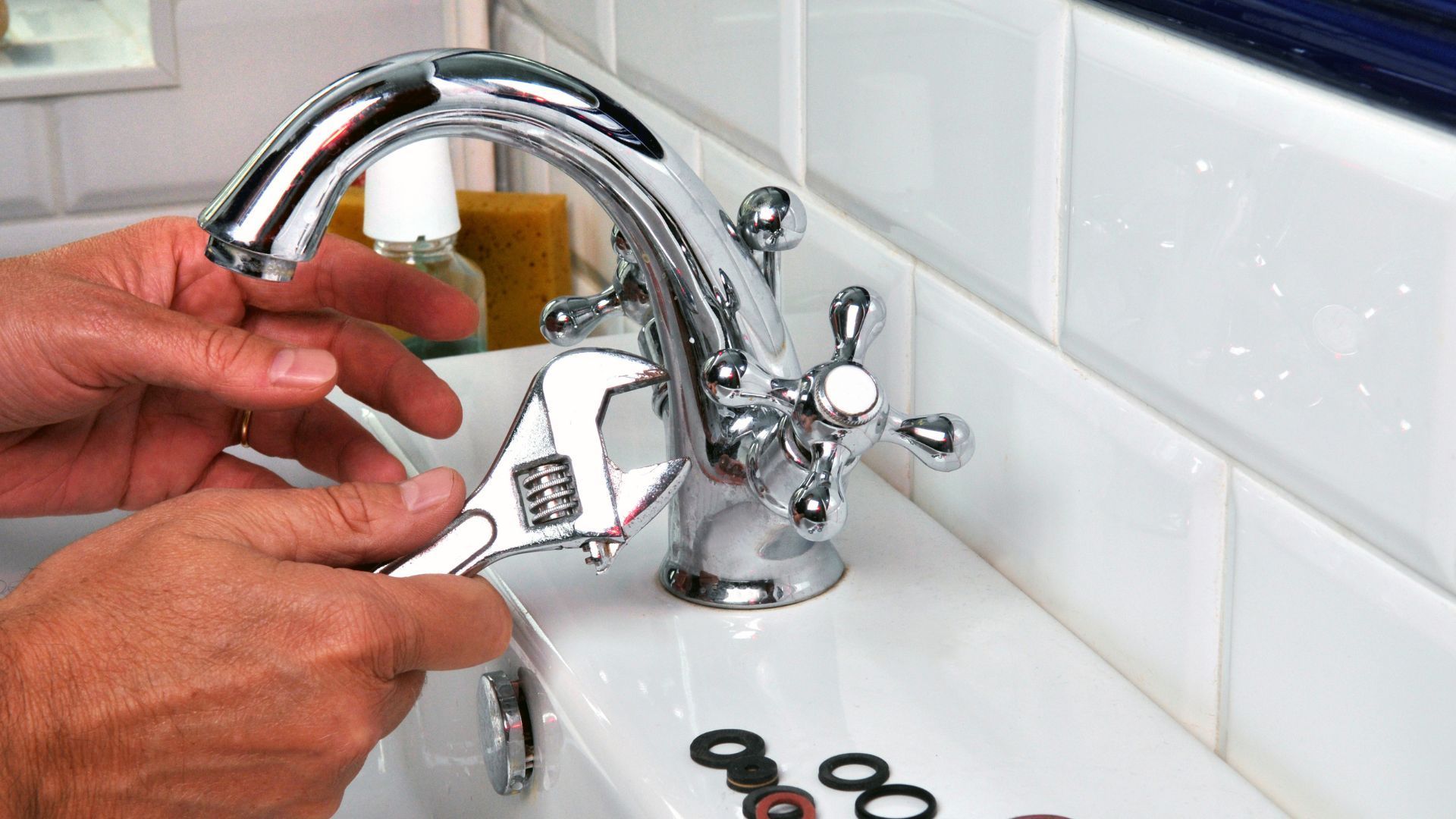 Hands using a wrench to tighten a chrome bathroom faucet on a white sink