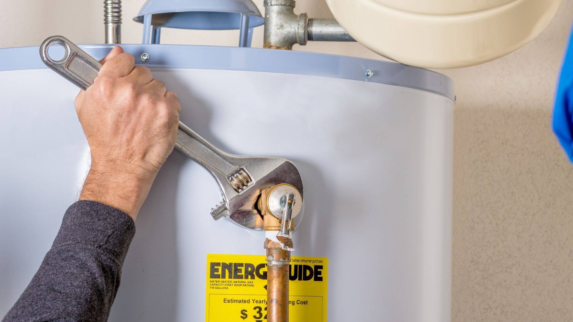 Hand tightening a wrench on a water heater control valve with an Energy Guide label.