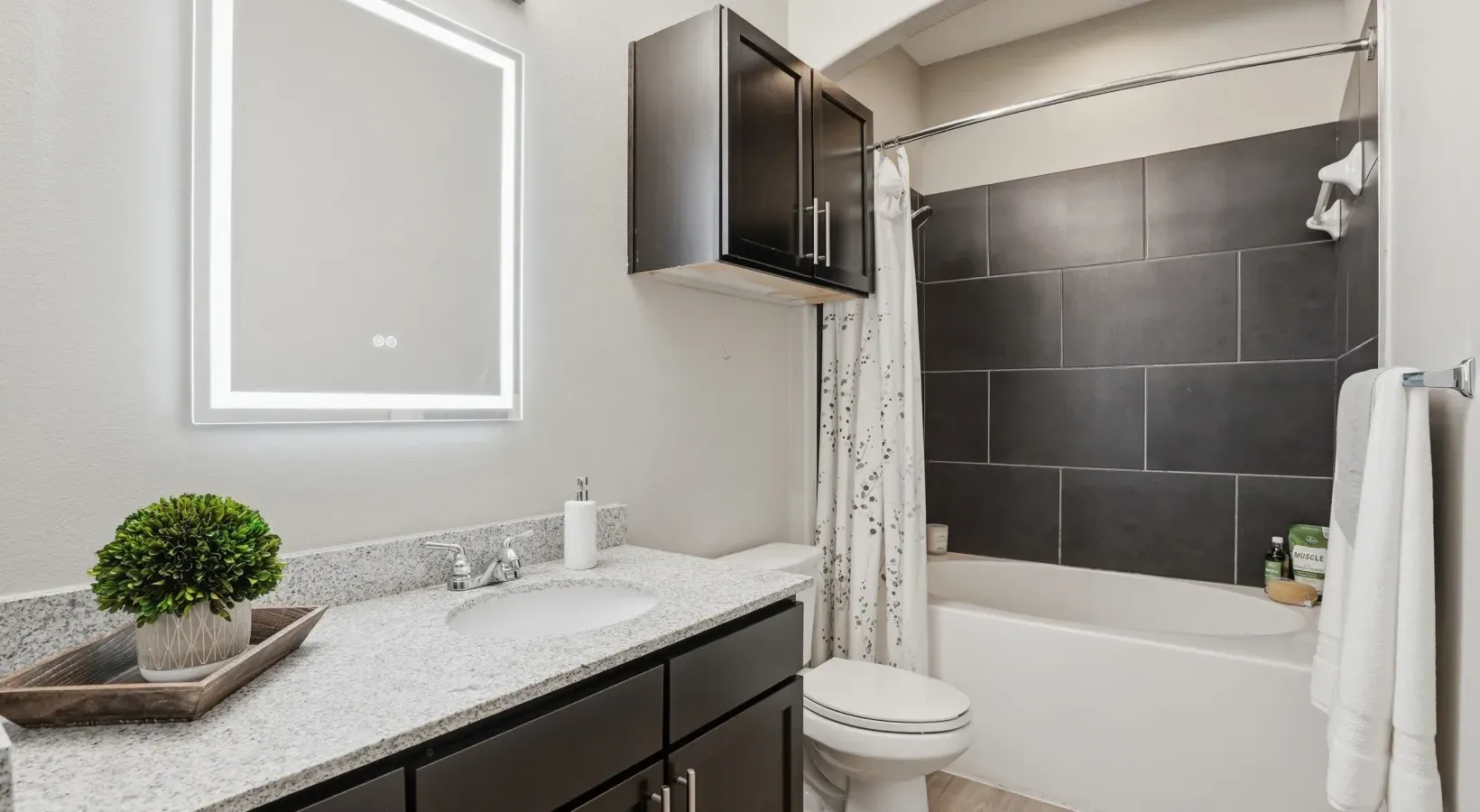 Modern bathroom with granite vanity, dark cabinets, wall mirror, and tiled shower at Layers Galleria.