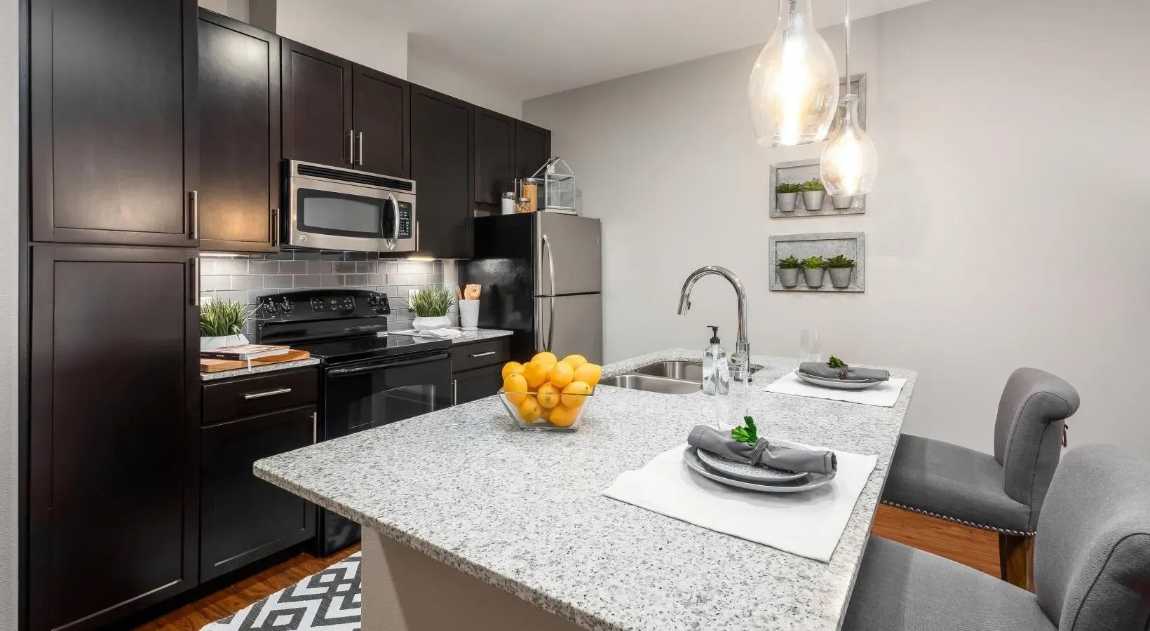 Modern kitchen with dark cabinets, white island, stainless appliances, and gray chairs at Layers Galleria.
