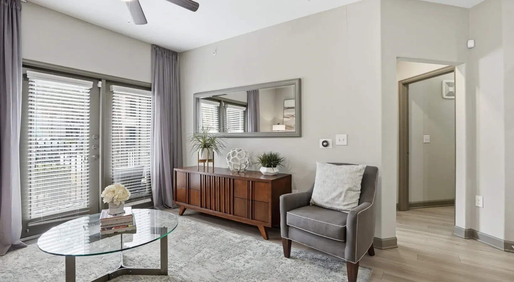 Bright living room with gray sofa, wood console, coffee table, and sliding glass doors to a patio at Layers Galleria.