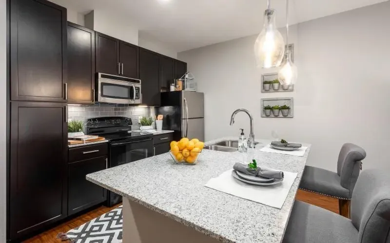 Modern kitchen with dark cabinets, stainless appliances, and a light granite island set for two at Layers Galleria.