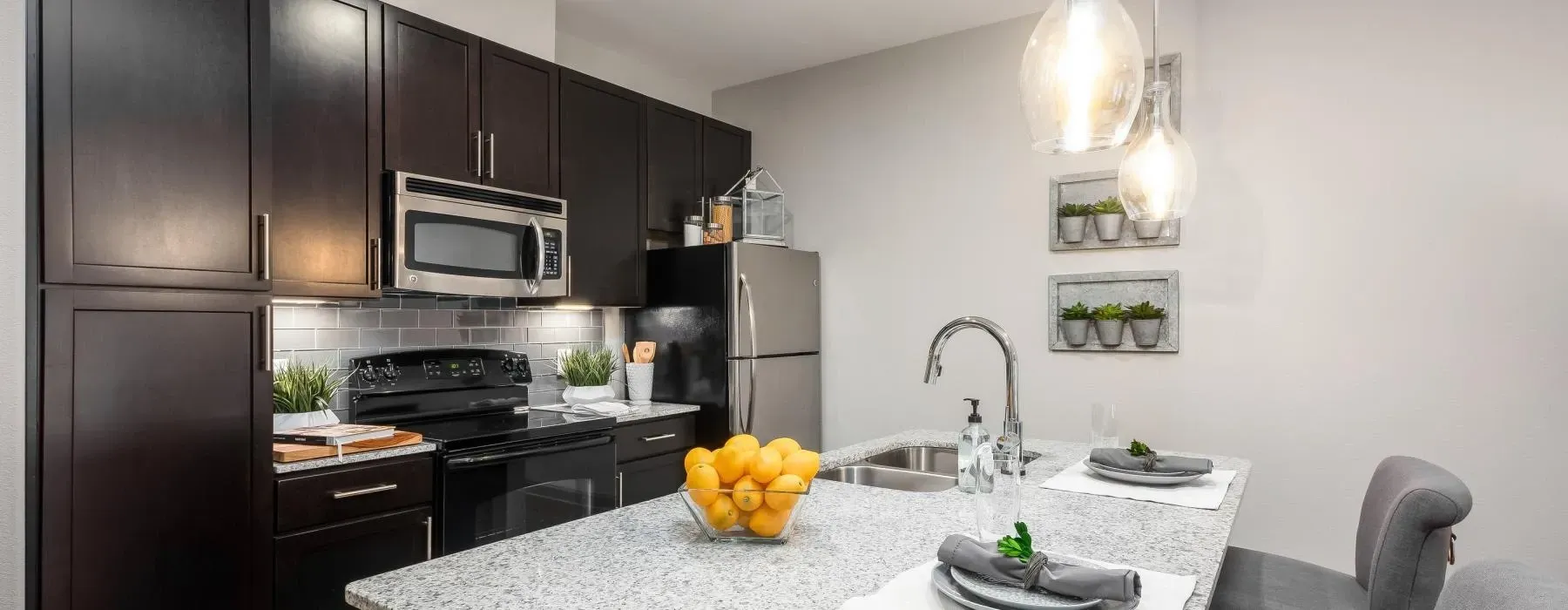 Modern kitchen with dark cabinets, stainless appliances, and a granite island with a bowl of lemons at Layers Galleria.