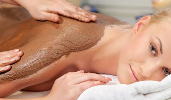 Woman receiving a chocolate body mask during a spa treatment, lying on a towel
