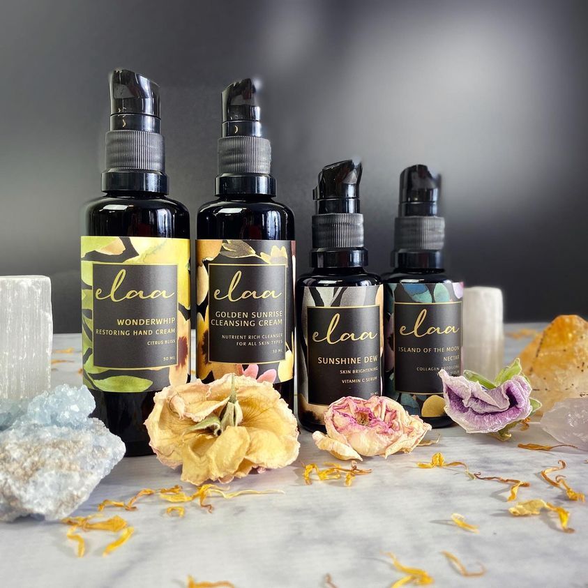 Four black essential oil bottles with floral labels and dried flowers on a marble surface